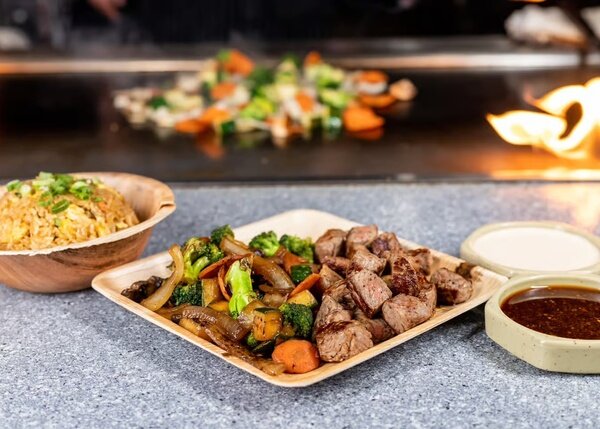 Hibachi steak cubes with vegetables, fried rice and two sauces, the grill flaming behind